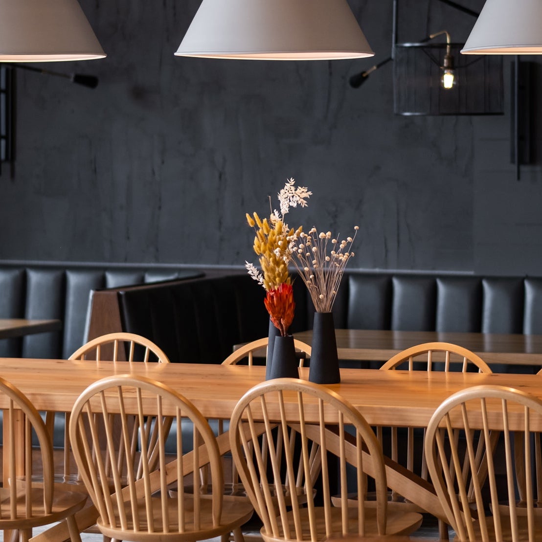 Long wooden table in Scandinavian inspired restaurant. Handcrafted wood booth tables with black leather.