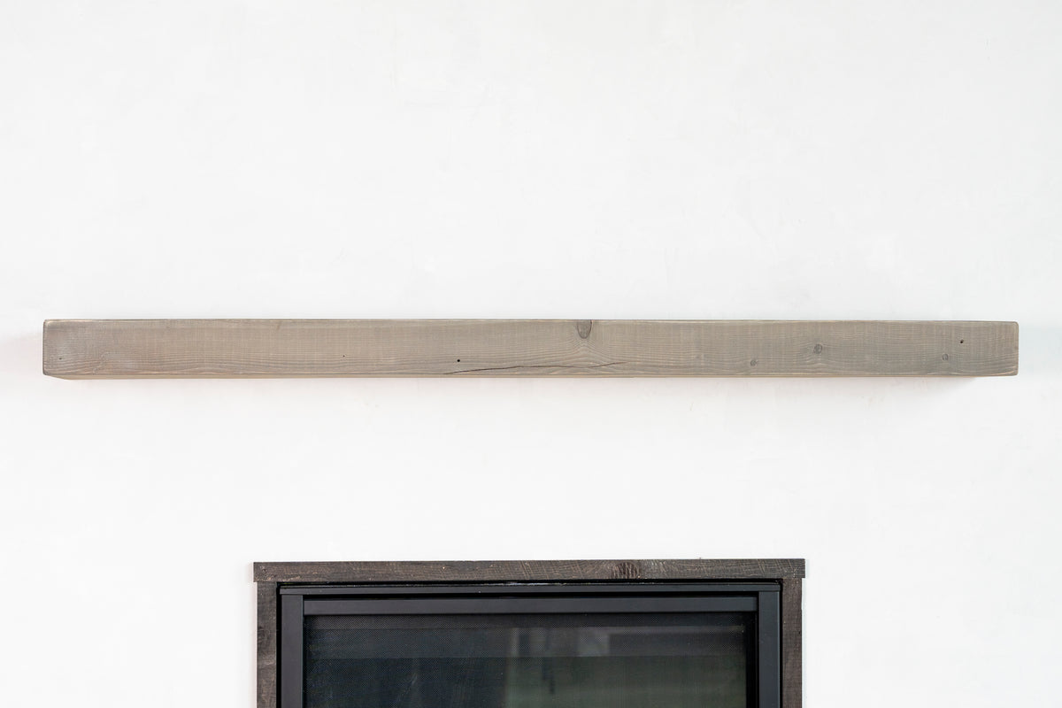 Wooden mantel shelf on a white wall above a fireplace.
