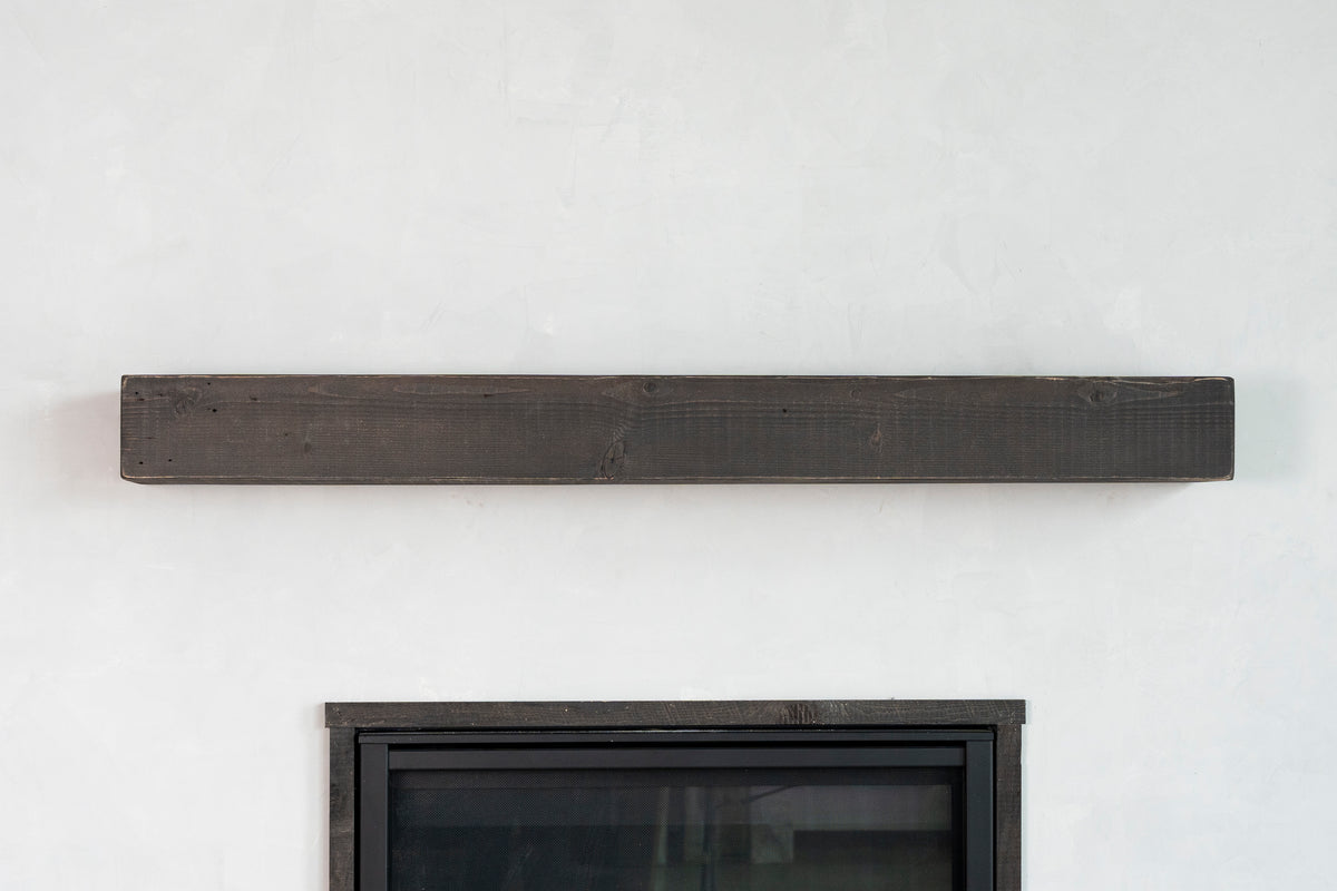 Long rectangular dark wood shelf mounted on a white wall above a fireplace.